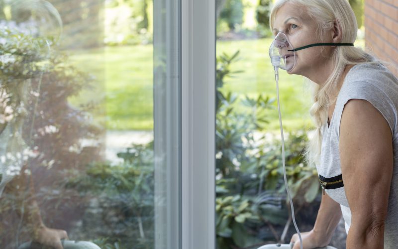Elder person with an oxygen breathing mask looking at a window