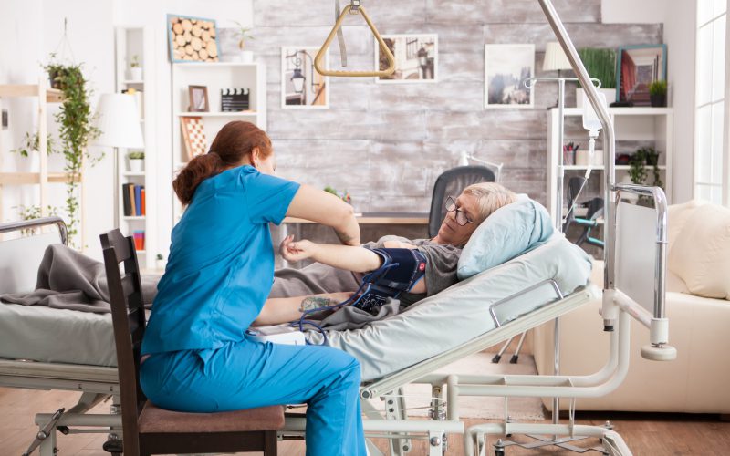 Young nurse checking the blood pressure of sick old woman in nursing home.